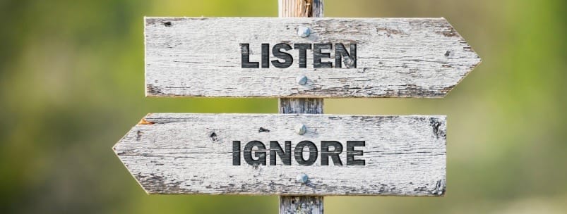 two wooden signs, one pointing left that says listen, the other pointing right that says ignore