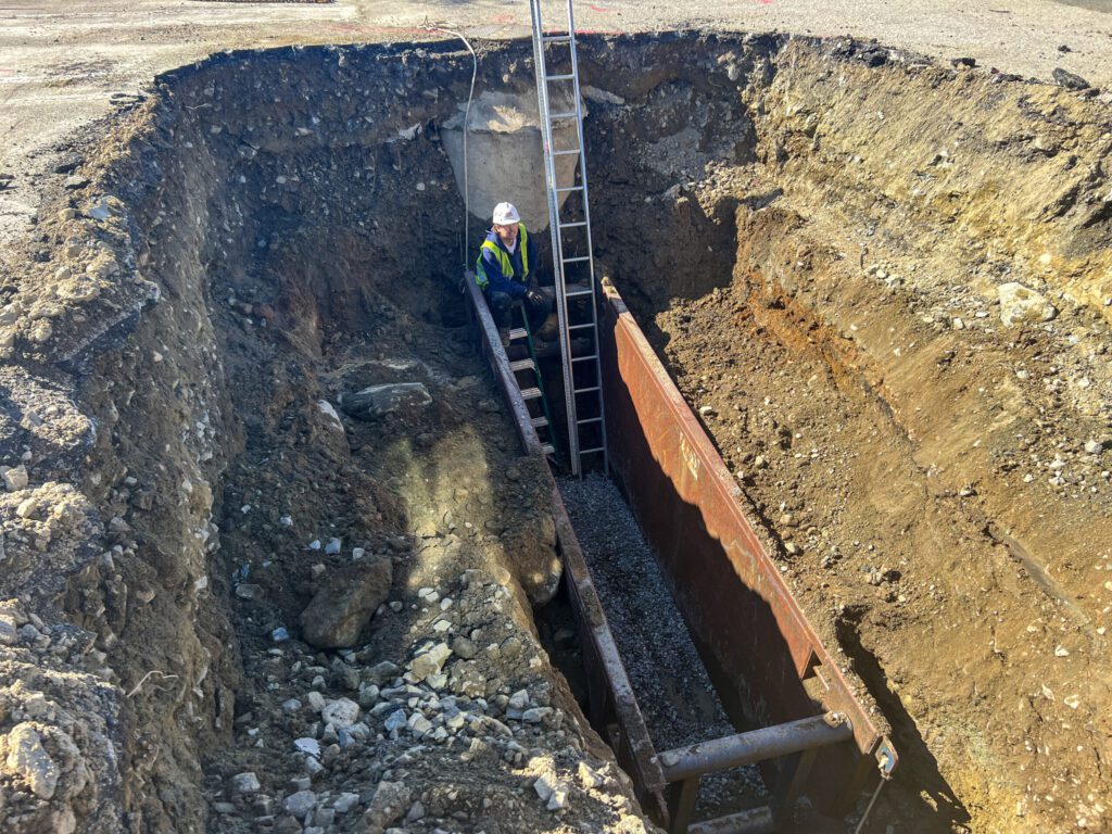 Construction trench with safety measures for OSHA compliance shows trench box for cave in protection